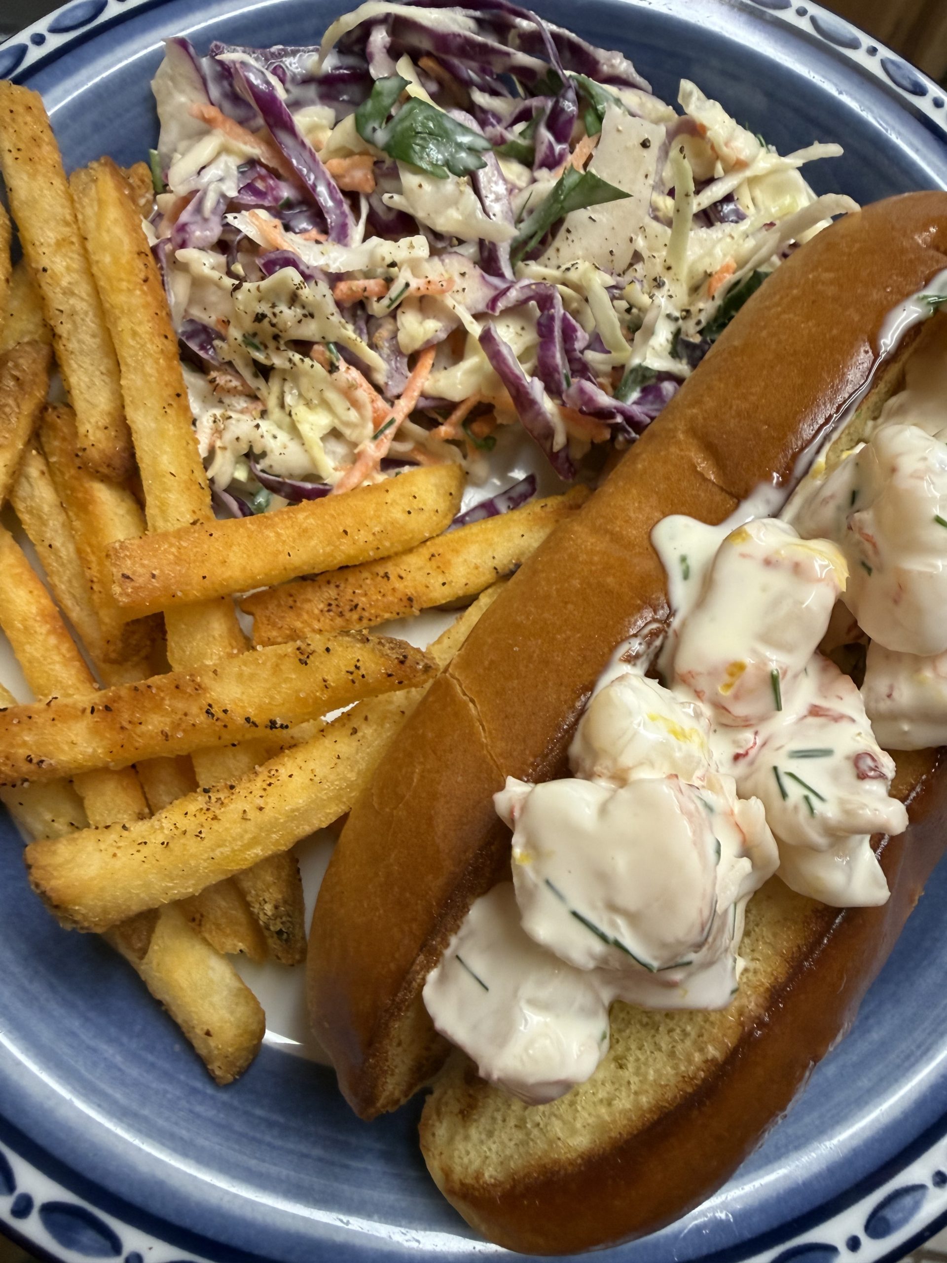 Shrimp roll on a brioche bun, seasoned fries and coleslaw on a plate
