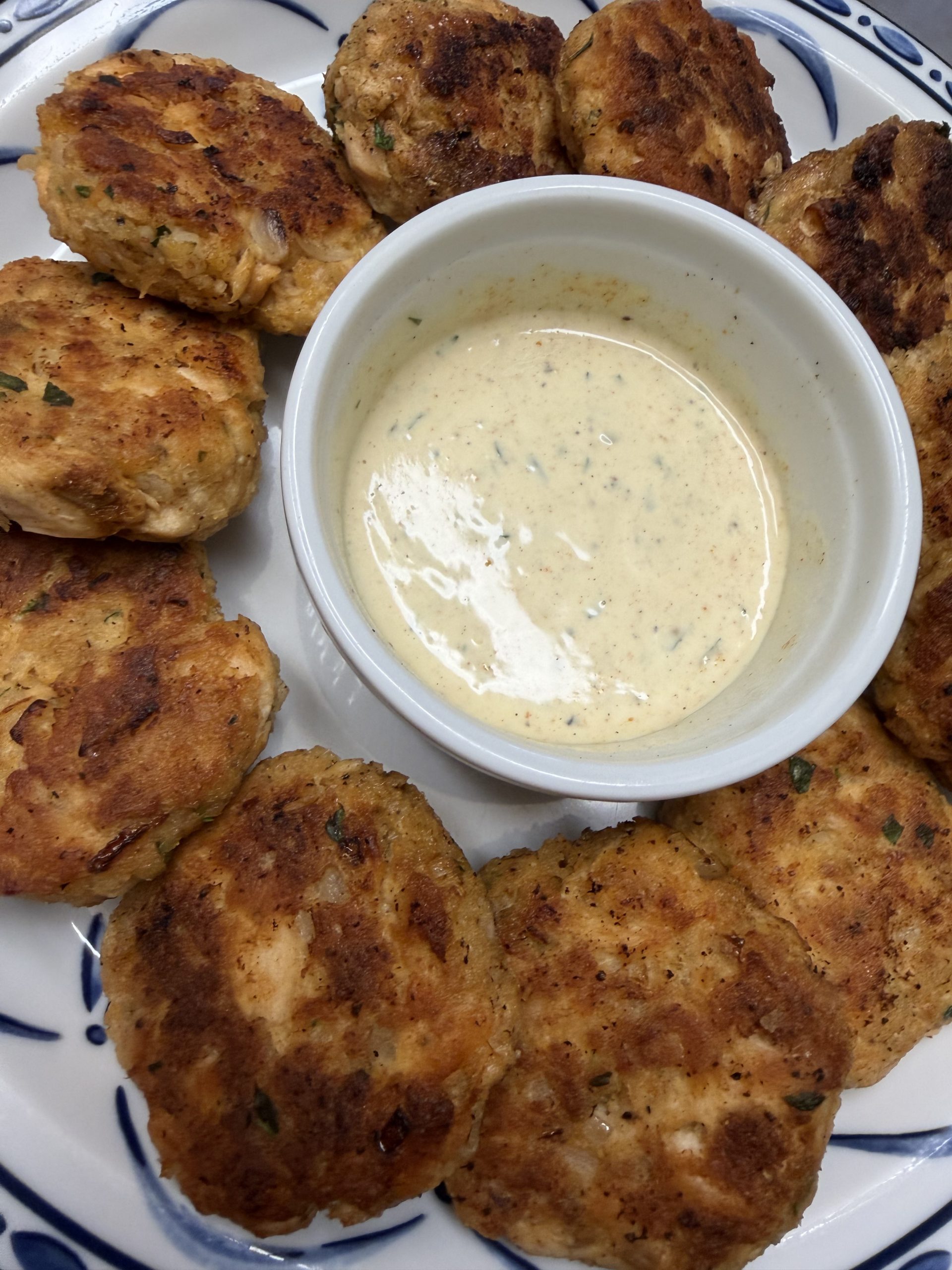 Salmon cakes plated on a circular plate with a lemon aioli in the middle
