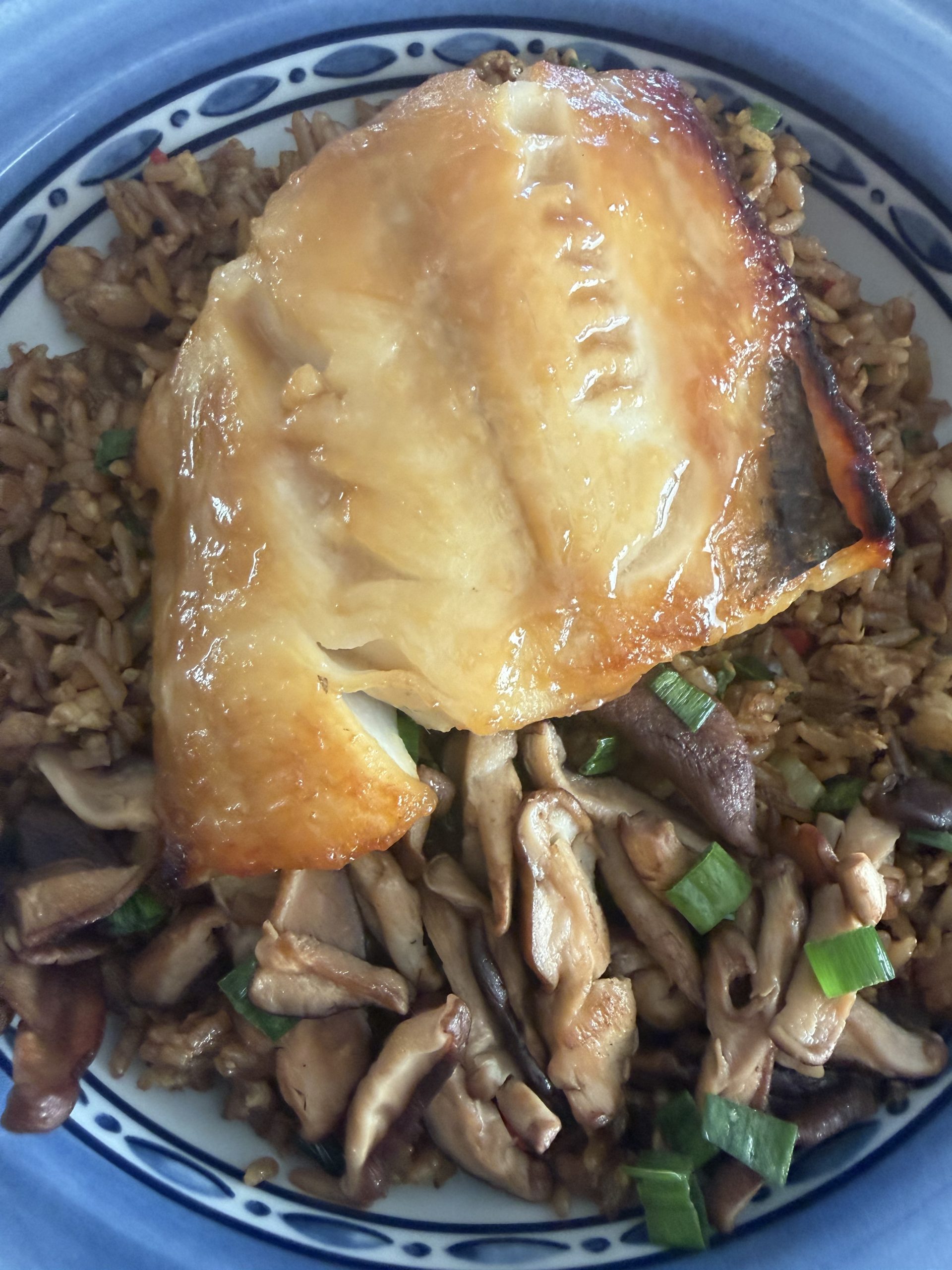 Plated miso marinated black cod on top of fried rice with a side of sautéed mushrooms